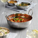 A Vollrath stainless steel balti dish filled with food on a table.