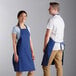 A man and woman wearing Choice royal blue adjustable bib aprons with pockets.