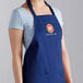 A woman wearing a blue Choice poly-cotton bib apron with a logo on it.