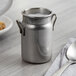 A stainless steel Vollrath mini milk can with a spoon on a table.