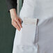A person wearing a Choice white poly-cotton bistro apron with a pen in the pocket.