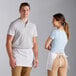 A man and woman wearing Choice white customizable standard waist aprons.