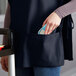 A person's hand putting a cell phone in the pocket of a navy blue cobbler apron.