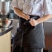 A woman wearing a Choice black poly-cotton 4-way waist apron in a professional kitchen.