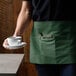 A person in a Choice hunter green apron holding a cup and saucer.