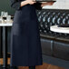 A woman wearing a navy blue bistro apron holding a tray.