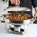 A person using a Vollrath Orion lift-off small oval chafer to serve meatballs outdoors.