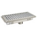 A stainless steel Advance Tabco floor trough with a fiberglass grating cover over the drain hole.