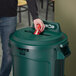 A man opening a green Rubbermaid recycling bin lid with a mixed recycle slot.