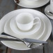 A white Libbey Royal Rideau tea cup and saucer on a white plate with silverware on a wooden table.