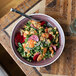 A Libbey Englewood matte mulberry porcelain bowl filled with kale salad, chickpeas, and radishes on a table with a spoon.
