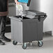 A gray mobile ice bin with a flip lid and caster wheels, designed for holding and transporting ice.