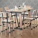 The Lancaster Table & Seating wooden bar height trestle table base with chairs and glasses on it.