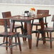 A Lancaster Table & Seating wooden dining height trestle table base on a wood table with chairs and wine glasses.