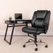 A black Flash Furniture Hercules Big & Tall mid-back office chair with wheels next to a glass desk.