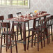 A Lancaster Table & Seating Mahogany wooden trestle table base for a bar table with wine glasses and chairs.