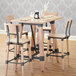 A Lancaster Table & Seating wooden bar height trestle table base with chairs and glasses on it.
