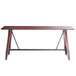 A Lancaster Table & Seating bar height trestle table with legs and a wooden top.