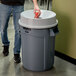 A man using a Rubbermaid BRUTE 32 gallon trash can with a funnel top to throw a can into it.