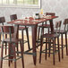 A Lancaster Table & Seating live edge bar height trestle table with chairs and wine glasses.