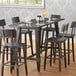 A Lancaster Table & Seating bar height table with a black rectangular top and chairs with wine glasses on a wood floor.