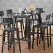 A Lancaster Table & Seating solid wood live edge bar height table with legs and an antique slate gray finish and chairs around it.