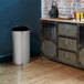 A Rubbermaid stainless steel open top trash can with a galvanized liner sits next to a metal cabinet in a home kitchen.