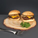 A cheeseburger and a hamburger on a Libbey faux wood slice porcelain serving board with a fork.