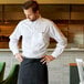 A man in a Henry Segal white long sleeve dress shirt and black apron standing at a restaurant counter.