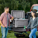 A man and woman standing next to a CaterGator outdoor cooler full of soda cans.