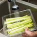 A hand washing celery in a Cambro clear colander pan over a sink.