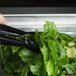 A person using Cambro black plastic tongs to serve lettuce at a salad bar.