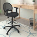 A Boss black mesh drafting stool with adjustable arms next to a desk.