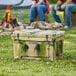 A CaterGator camouflage outdoor cooler on grass with people sitting on logs.