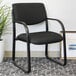 A black Boss fabric guest chair with armrests next to a plant.