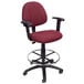 A burgundy Boss drafting stool with a black metal base and black adjustable arms.