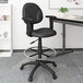 A black Boss drafting stool with a metal base next to a desk.