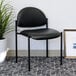 A Boss Diamond Black Caressoft Vinyl Stacking Chair in a lounge area with a plant in a white pot.