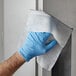 A person in blue gloves using 3M Stainless Steel Hood Degreaser wipes to clean a door.