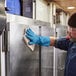 A man in blue gloves using 3M Scotch-Brite Stainless Steel Hood Degreaser wipes to clean a stainless steel refrigerator.