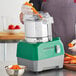 A person using an AvaMix stainless steel food processor to chop a carrot.