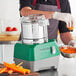 A person using an AvaMix stainless steel food processor to shred carrots.