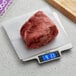 A piece of raw meat on a Taylor stainless steel digital kitchen scale.