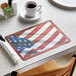 A patriotic paper placemat on a table with a coffee cup on a saucer.