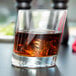 A Libbey customizable slanted rocks glass with whiskey and ice on a table.