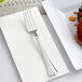 A Visions silver plastic fork on a napkin next to a plate of food.