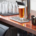 A Regency stainless steel beer drip tray with rinser on a counter with a glass of beer.