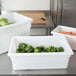A white Rubbermaid food storage box on a kitchen counter filled with green peppers.