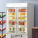 A Beverage-Air white glass door merchandiser freezer with shelves full of food.