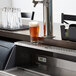 A Regency stainless steel underbar mount beer drip tray catching beer from a tap over glasses on a counter.